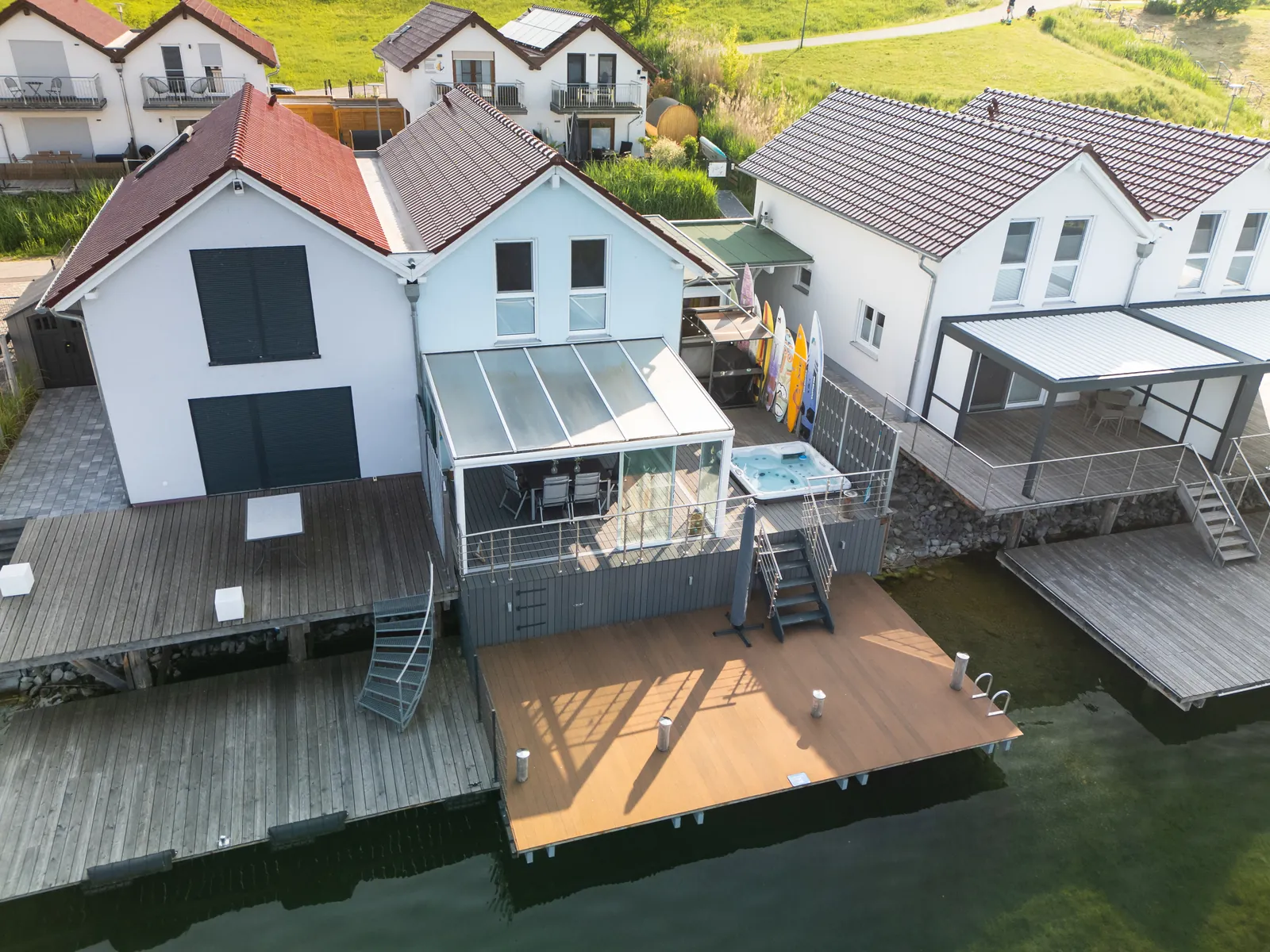 Luftaufnahme: Terrasse mit Whirlpool, Stand-up-Boards und großer Steg direkt am Wasser